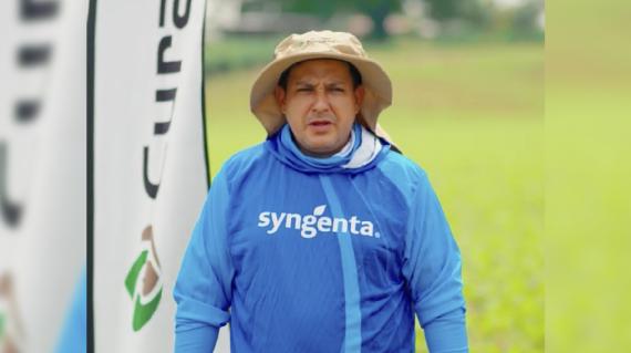 Hombre con sombrero y sudadera azul “syngenta” en un campo verde