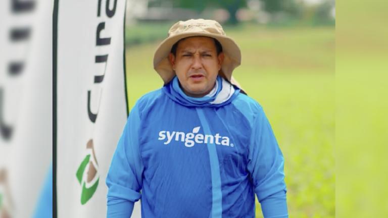 Hombre con sombrero y sudadera azul “syngenta” en un campo verde